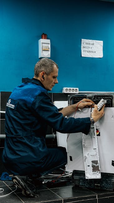 The image shows a technician in a dark blue uniform kneeling next to an open electrical panel or appliance, possibly performing maintenance or repairs. He is holding a digital multimeter or testing de